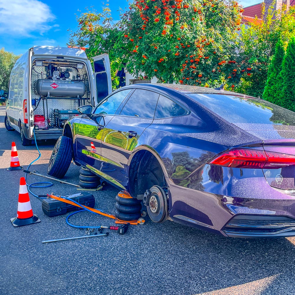 Mobilna wulkanizacja w słoneczny dzień wymienia przy drodze opony w fioletowym samochodzie Audi A7