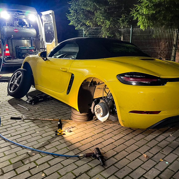 Mobilna wulkanizacja wymienia opony w nocy w żółtym samochodzie kabriolet Porsche