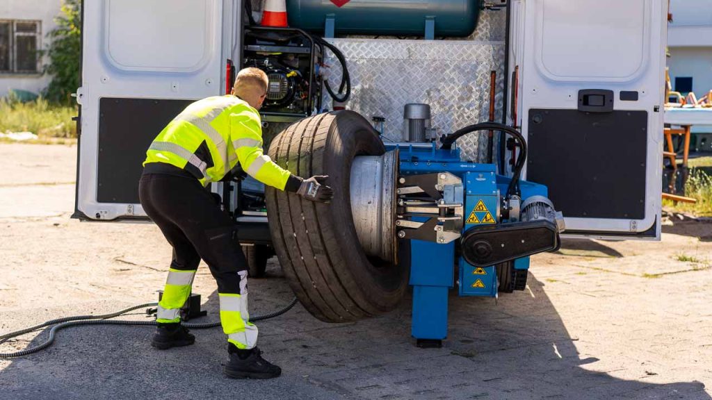 Serwisant zdejmuje oponę ciężarową z felgi na mobilnej montażownicy w busie serwisowym